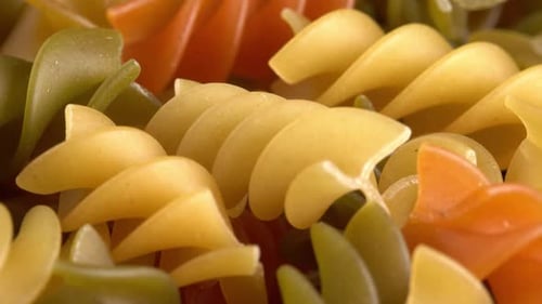 Multicolored italian pasta Fusilli or Rotini rotating in macro background side view. Durum wheat