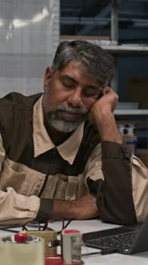 Exhausted Mature Asian Warehouse Worker Nodding Off by Laptop