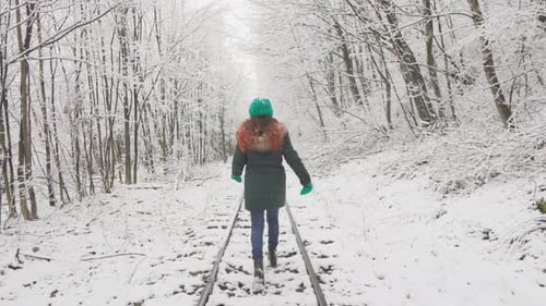 Woman Walking on Railroad Tracks in Snowy Forest