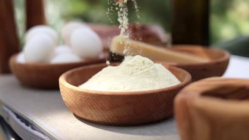 Hand sprinkles grated cheese in bowl
