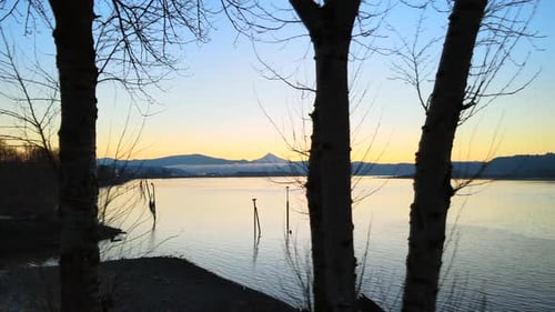 Drone slowly panning to the right and revealing beautiful scenic view of a large lake during sunset.