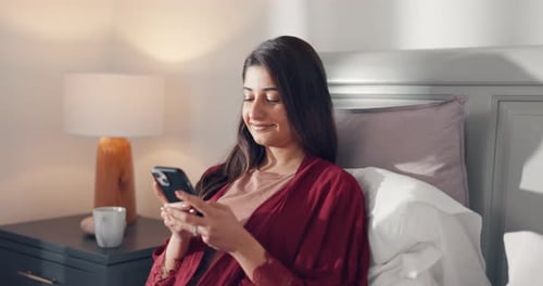 Woman Smiling and Using Phone in Bed at Home