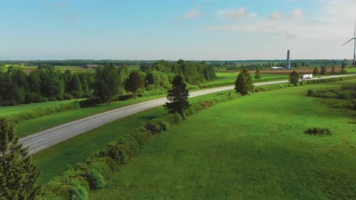 Aerial View of White Semi Trucks with Cargo Trailers Moving on the Highway. In the Background Windm