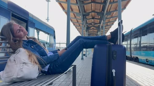 A Woman Sleeps on the Platform of the Railway Station with Luggage She is Waiting for Her Train