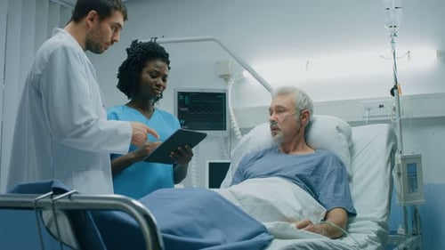 In the Hospital, Senior Man Lying in the Bed, Talks with Doctor and Nurse who Use Tablet Computer.