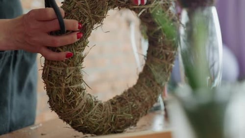 Woman Trims Dried Grass Wreath with Scissors at Table