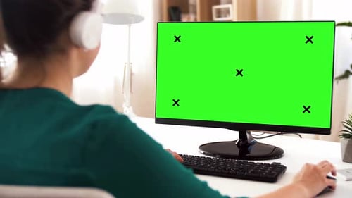 Woman in headphones works on chroma key green screen computer at home office