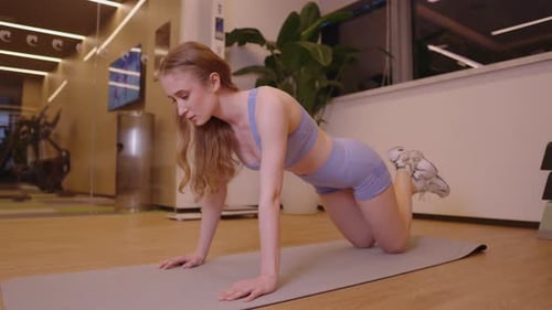 Determined Young Woman with Long Blonde Hair Doing Knee Push Ups on a Yoga Mat in a Modern Gym