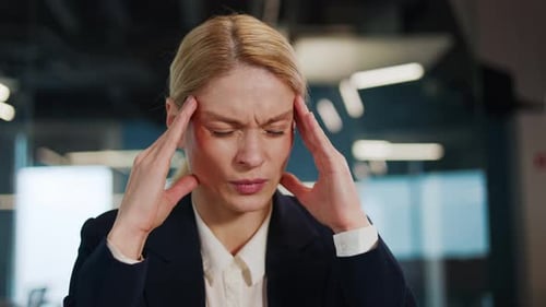 Exhausted Stressed Overworked Businesswoman Experiencing a Headache in Office