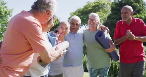 Diverse group of happy male and female seniors talking after exercising in sunny garden, slow motion