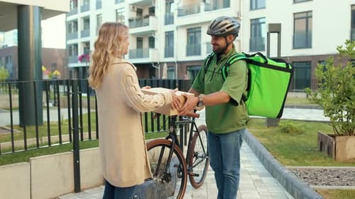 Close Up Young Man Courier in a Safety Helmet Delivering Box to the Customer Home By Bicycle