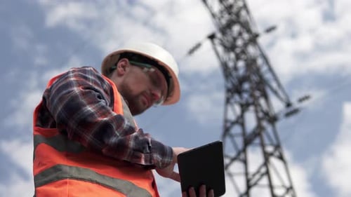 Engineer Using Tablet Device Near Power Tower