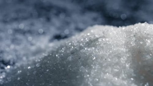 Nahaufnahme auf schwarzem und blauem Hintergrund liegt auf weißen, krümeligen granulierten Zuckerkristallen darüber. Gießen Sie auf eine