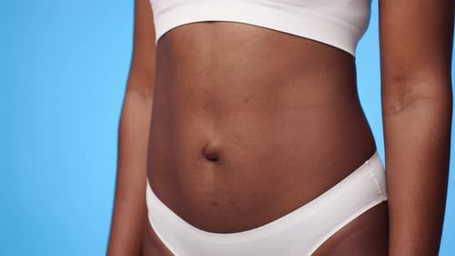 Junge Frau posiert mit nacktem Bauch vor einem leuchtend blauen Hintergrund