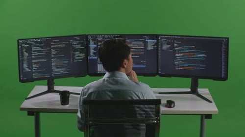 Back View Of Asian Man Thinking While Write Code With Multiple Computer Screens In Green Screen