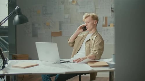 Ingénieur confiant avec des dessins au bureau passant un appel téléphonique pour discuter d'un projet