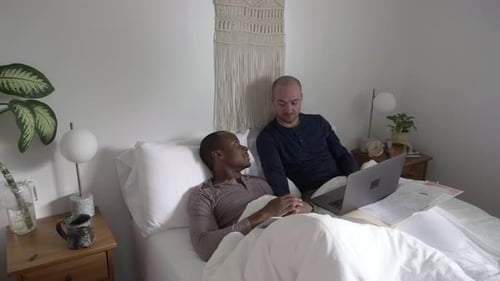 Two men work in bed on laptop