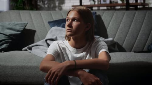 Young Person Sitting on a Modern Sofa Indoors with a Thoughtful Expression