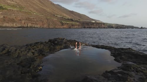 Aerial View Capturing Adventurous Traveler Plunging Into Turquoise Volcanic Pool Against Dramatic