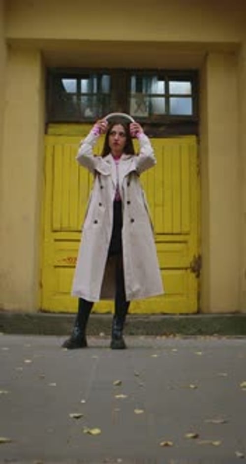 Mujer con gabardina y auriculares cerca de la puerta amarilla