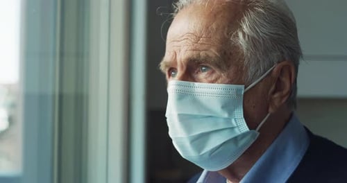 Cinematic close up shot of an elderly thoughtful man wearing protective medical mask is looking th