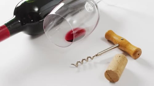 Red wine bottle, empty glass, cork and corkscrew lying on white surface with copy space