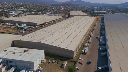 Aerial view of industrial buildings, warehouses with trucks around and moving vehicles, sunset