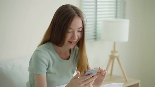 Smiling Woman Using Smartphone in Bright Bedroom