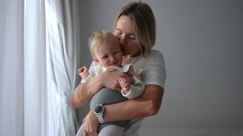 Loving Mother Holding Happy Baby Indoors by Window