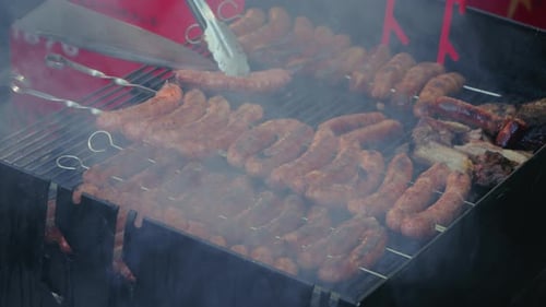 Close-up of grilling sausages on an outdoor barbecue grill in summer, preparing over smoky charcoal.
