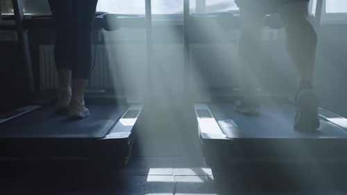 Closeup of Legs Walking on a Treadmill in Rays of Light