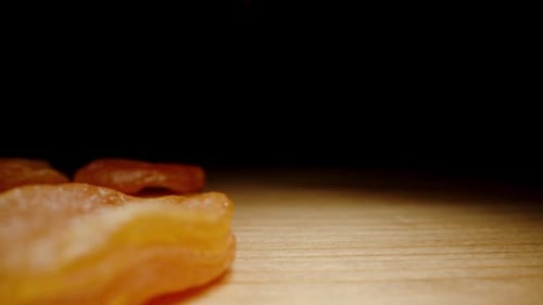 Dried Apricots Falls onto a Wooden Table Against a Black Background, in Slow Motion. Dolly slider.