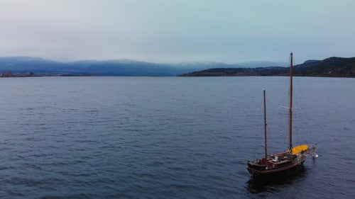 Smooth flying drone beside sailboat on mountain lake