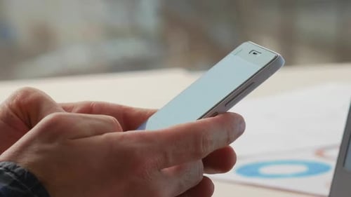 Hands Hold Smartphone Next to Laptop with Charts