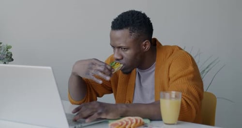 Man Working at Computer, Eating Sandwich
