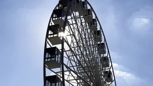 Blick auf ein Riesenrad vor einem klaren blauen Himmel mit Sonnenlicht im Hintergrund Die Sonnenstrahlen ziehen vorbei