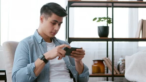 Young Adult Gaming on Smartphone in a Home