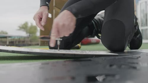 Man Assembling Wakeboard with Wrench on Grassy Field
