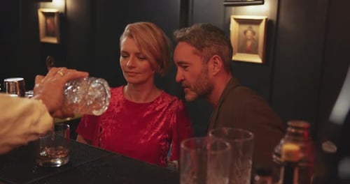 Couple drinking tasting cocktails in bar at night with bartender