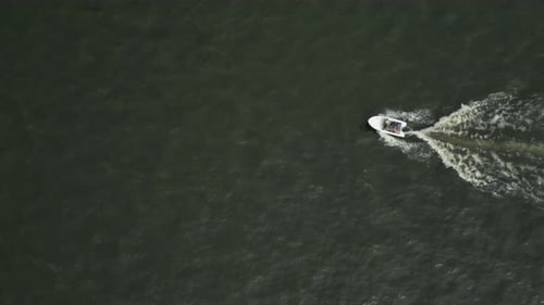 A small boat moving across open water leaving a trail behind it, aerial view