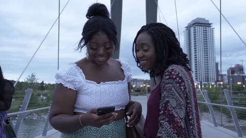 Friends Smiling and Looking at Mobile Phone on Bridge