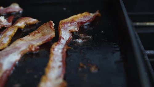 Extreme close up of sizzling bacon frying on grill, selective focus