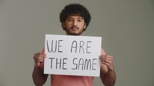 Ein seriöser indischer Aktivist mit direktem, selbstbewusstem Blick hebt Hände und zeigt Poster