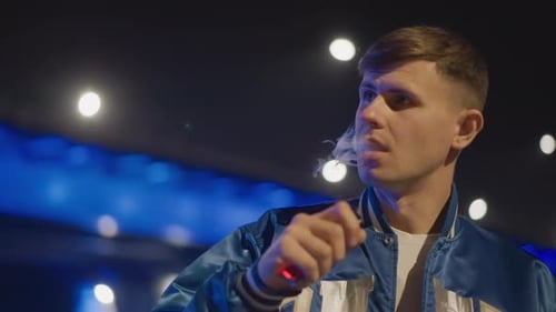 Nighttime Shot of Man Exhaling Vapor Against Vibrant Neon Backdrop Close Shot of Male Engaging in