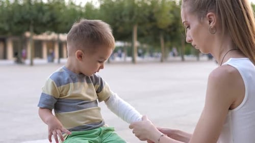 Young Mother Comforting Her Little Son and Giving Him Bandage in a Wounded Hand After Getting Hurt