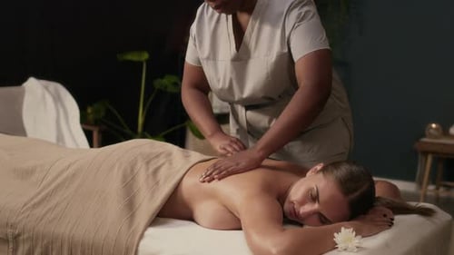 Masseurin reibt Frau vor der therapeutischen Massage im Spa-Raum den Rücken