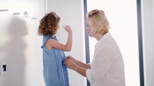 Mother buttoning up blue dress on young girl