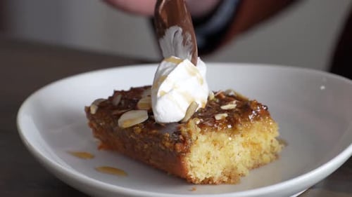 Person Eating A Slice Of Banana Caramel Cake Topped With White Icing In A Restaurant. - Closeup Shot