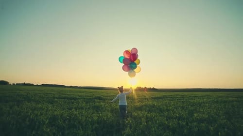 Girl Walks with Balloons in Green Field at Sunset