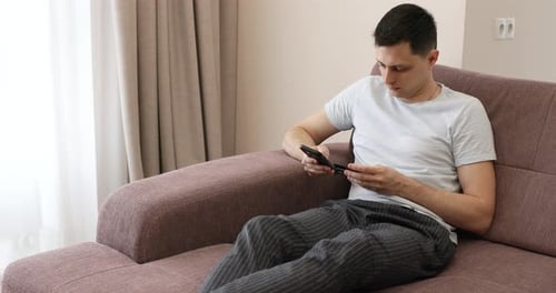 Young Adult Using Phone Relaxing on Couch Indoors